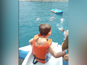 A child in a life jacket prepares to join friends swimming in vibrant blue waters, capturing the essence of fun water activities during a boating adventure.