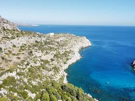 A stunning aerial view of a rocky coastline meeting the clear blue waters, showcasing the natural beauty of the landscape — perfect for exploring by boat.