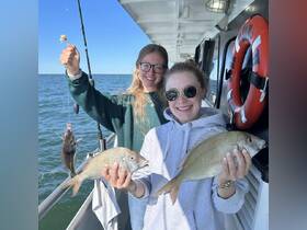 Two friends proudly display their catch while fishing on a boat, showcasing a fun day of on-water activities and camaraderie.