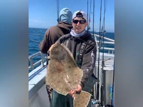 A proud angler displays a freshly caught flounder while fishing on a boat, showcasing the excitement of ocean fishing adventures.
