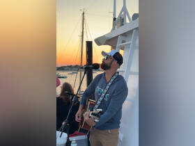 A musician performs live on a boat during sunset, creating a vibrant atmosphere for guests to enjoy the evening.