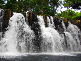 A scenic view of a waterfall cascading over rocks, surrounded by lush greenery, creating a tranquil natural setting.