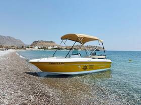 A vibrant yellow speedboat rests on a pebbled beach, showcasing the stunning Aegean coastline — perfect for summer adventures and boat rentals.