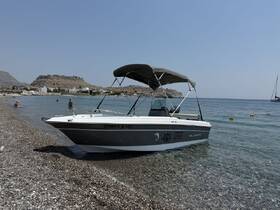 A sleek speedboat rests on the pebbled shore of a tranquil beach, with swimmers enjoying the clear waters in the background — a perfect spot for summer adventures.
