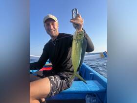 A happy angler proudly displays his catch of the day, showcasing a vibrant fish against the backdrop of the open ocean — a perfect moment for fishing enthusiasts.