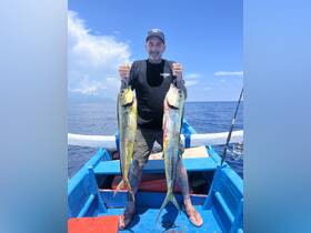 A proud angler displays his impressive catch of two mahi-mahi while aboard a fishing boat in the open ocean — a thrilling moment for fishing enthusiasts.