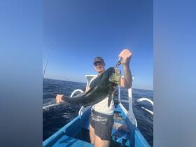 A fisherman proudly displays his catch aboard a boat in the open ocean, showcasing the thrill of deep-sea fishing adventures.