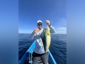 A proud angler holds up a vibrant catch while fishing on the open ocean, showcasing the thrill of deep-sea fishing adventures.