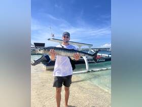 A proud angler holds up his impressive catch while standing in shallow water near a fishing boat, showcasing the thrill of a successful fishing trip.