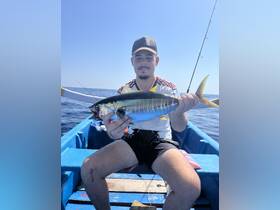 A proud angler displays his catch aboard a small boat in the open ocean, showcasing the thrill of fishing adventures.