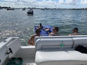 A group of friends enjoys a sunny day on the water, lounging on a floating mat while a boat approaches in the background — perfect for summer fun and relaxation.