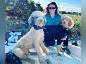 A woman poses with her two dogs on a boat, enjoying a sunny day in nature — perfect for pet-friendly boating adventures.