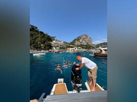 A lively group enjoys a fun day swimming in crystal-clear waters, with a boat in the foreground — perfect for summer adventures and celebrations.