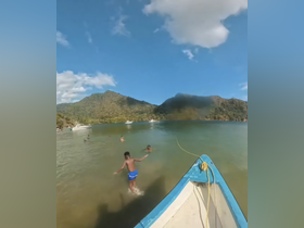A group of children enjoys a fun day swimming in clear waters, with a picturesque backdrop of mountains and boats — perfect for family adventures.