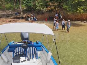 A lively group enjoys a beach stop near their boat, engaging in conversation and fun activities in the shallow water — a perfect day for relaxation and camaraderie.