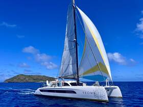 A stunning catamaran named 'YEOMA' sails through vibrant blue waters, showcasing its sleek design against a picturesque island backdrop.