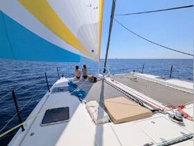 Two guests relax on the deck of a catamaran while sailing on the open ocean, enjoying the sun and sea breeze — a perfect moment for a sailing adventure.