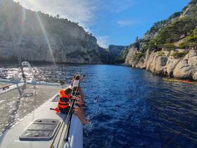 A group of children enjoy a scenic day on a catamaran, with stunning cliffs in the background and kayakers exploring the coastline — a perfect family adventure on the water.