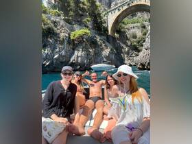 A lively group enjoys a sunny day on a boat, celebrating and having fun against a stunning coastal backdrop.