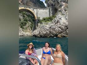 A joyful group of friends enjoys a sunny day on a boat, capturing the essence of a perfect beach outing against a stunning rocky backdrop.
