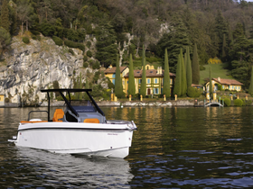 A sleek speedboat glides through calm waters, showcasing its modern design against a picturesque lakeside backdrop of lush greenery and charming villas.