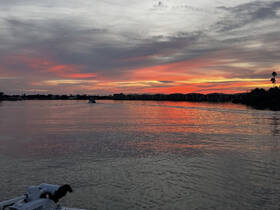 A stunning sunset reflects on the calm waters, with a boat gently cruising through the serene waterway, creating a picturesque scene perfect for evening outings.