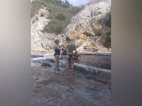 A group of friends enjoys a mud bath experience, surrounded by natural rock formations — a perfect way to relax and rejuvenate during a tropical getaway.
