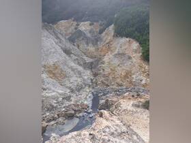 An unclear view of a rocky landscape with a stream, possibly indicating geothermal activity. The image lacks clarity and detail.