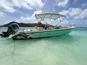 A sleek speedboat named 'Enbali' anchored in crystal-clear waters, showcasing its stylish design against a picturesque backdrop of hills and clouds.