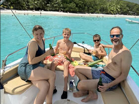 A joyful family enjoys drinks and snacks aboard a boat, surrounded by stunning turquoise waters and a beautiful beach backdrop — perfect for memorable family outings.