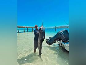 A proud angler displays a freshly caught marlin in shallow waters, showcasing the thrill of fishing in a tropical paradise.