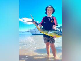 A young boy proudly displays his catch of the day, a vibrant fish, while standing in shallow water — a memorable moment from a fishing adventure.