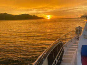 A serene sunset view from the deck of a boat, showcasing the tranquil waters and silhouetted hills — perfect for evening cruises.