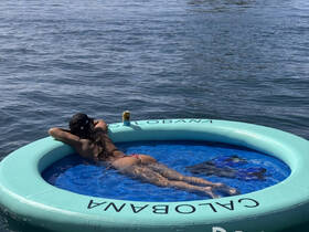 A woman relaxes on a floating mat in the water, enjoying a drink — the perfect setup for a day of leisure on the water.