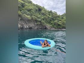 A woman enjoys a relaxing moment on a floating mat in the ocean, surrounded by lush greenery — perfect for a fun day on the water.