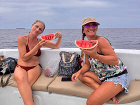 Two friends enjoy fresh watermelon slices while relaxing on a boat, capturing a fun moment on the water.