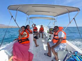 A cheerful group enjoys a boat ride on the ocean, all wearing life jackets and capturing the moment with smiles. Perfect for family outings or adventure tours.