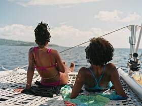 Two friends relax on the deck of a catamaran, enjoying the ocean view and sunshine — a perfect moment for unwinding on a sailing adventure.