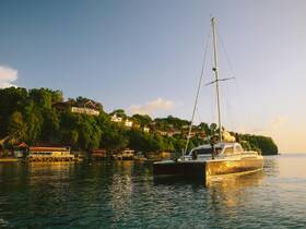 A catamaran glides through calm waters at sunset, with guests enjoying the scenic coastline — an ideal setting for a memorable sailing experience.