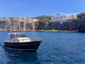 A charming boat navigates the clear waters near a stunning coastal town, showcasing the beautiful architecture and vibrant beach scene in the background.