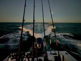A scenic view from the back of a fishing boat, showcasing fishing rods and the wake created as it moves through the water — perfect for fishing enthusiasts and adventure seekers.