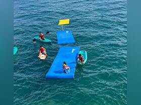 A group of children and adults enjoy a fun-filled day on the water with kayaking and a floating mat, perfect for summer adventures.