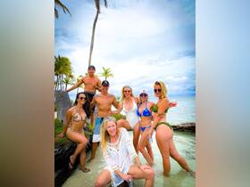 A lively group of friends poses for a fun beach photo, showcasing their vibrant swimsuits and drinks — perfect for celebrating a day in paradise.