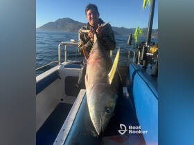 A proud angler displays a large tuna catch aboard a fishing boat, showcasing the thrill of deep-sea fishing in stunning waters.