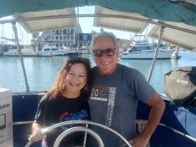 A cheerful couple poses at the helm of their boat, enjoying a sunny day at the harbor — perfect for creating lasting memories on the water.