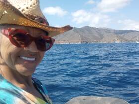 A smiling woman enjoys a sunny day on the water, with beautiful mountainous scenery in the background — a perfect moment for adventure and exploration.