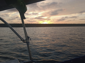 A serene sunset view from the deck of a boat, showcasing the tranquil waters and a distant shoreline — perfect for peaceful evening cruises.