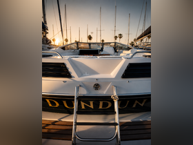 A stunning view of the back of a yacht named 'DUNDUN' docked at sunset, showcasing its sleek design against a backdrop of masts and palm trees.
