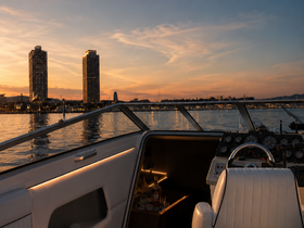 A serene view of the boat's helm at sunset, showcasing elegant interior design and a stunning backdrop of city skyscrapers reflecting on the water.