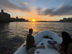 A couple enjoys a romantic sunset cruise on a boat, with stunning views of the shoreline and vibrant colors reflecting on the water.